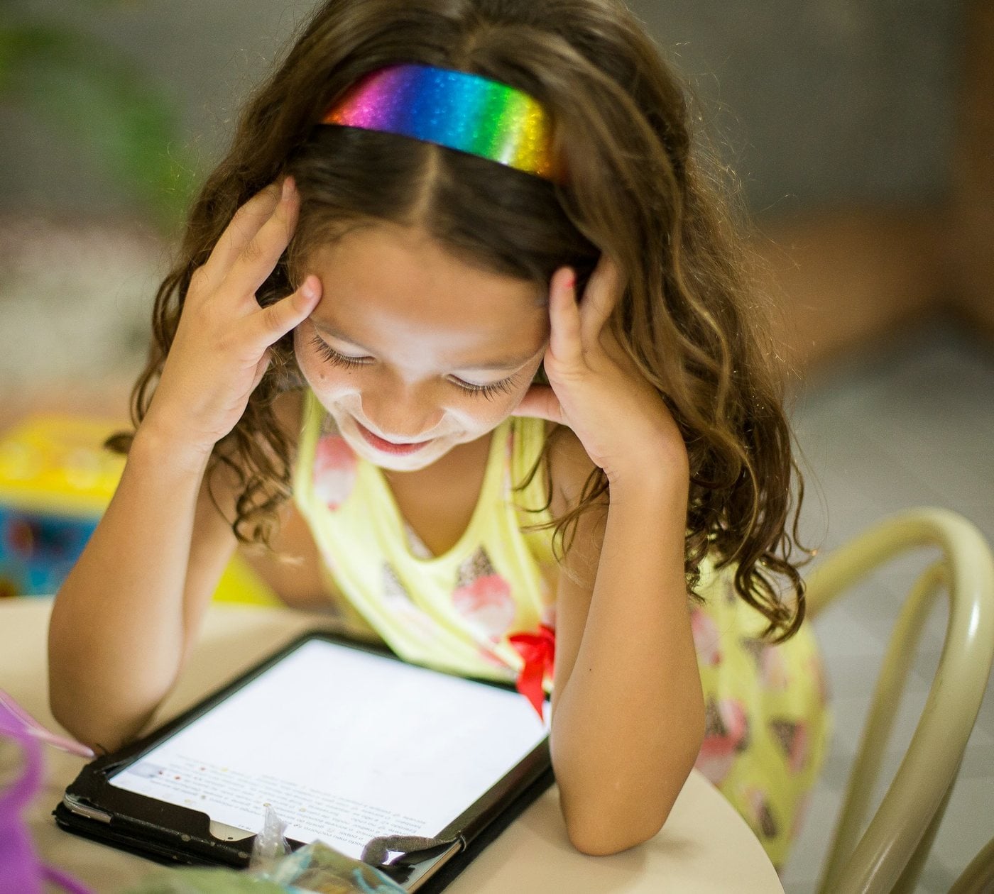 Una niña con una diadema de colores sonríe mirando una tableta